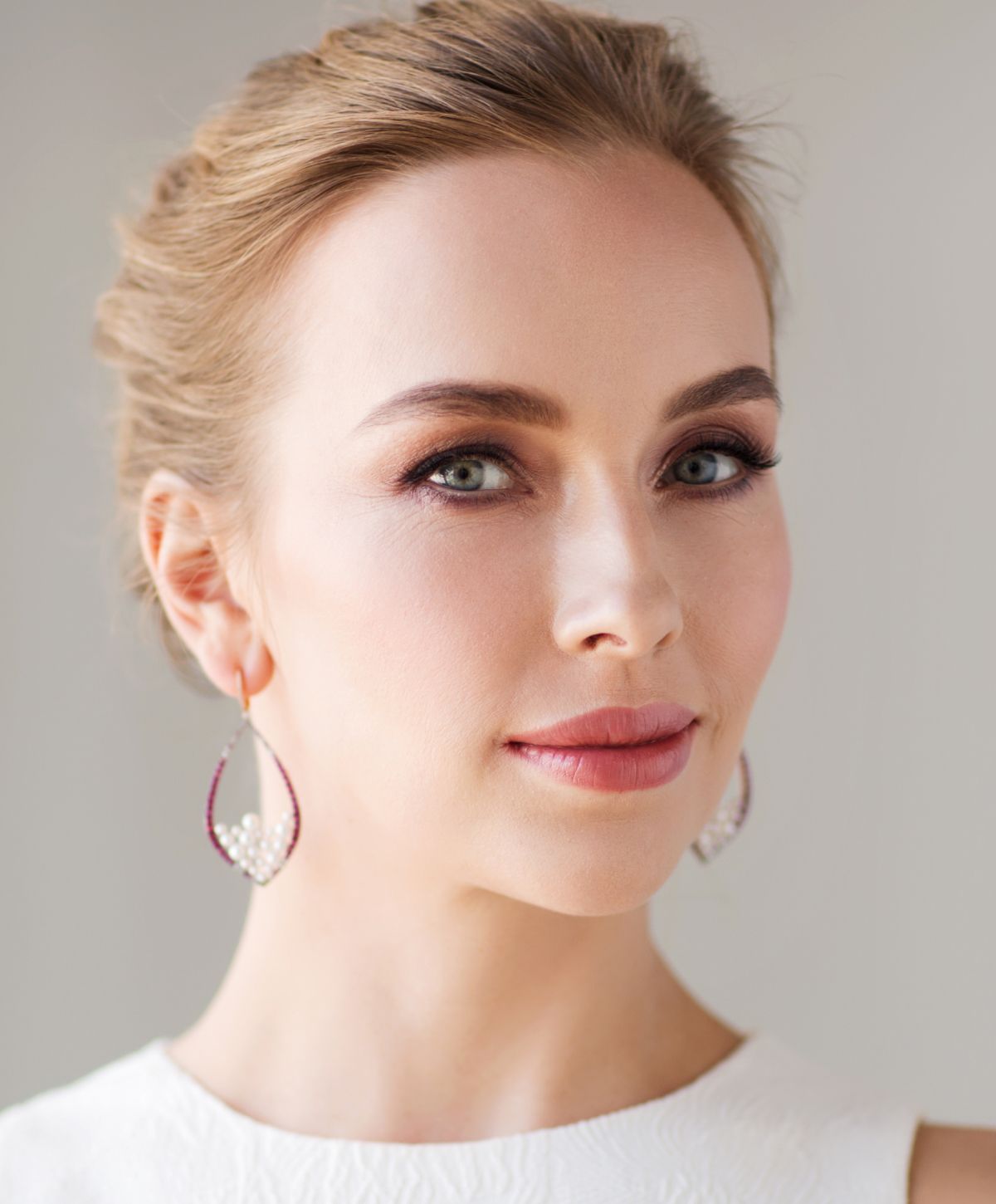 sculptra patient model wearing a white dress and earrings smiling softly